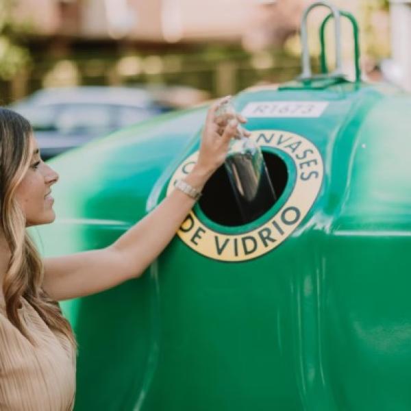 Una mujer depositando una botella de vidrio en el contenedor verde.