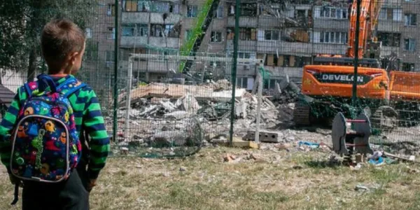 Un niño pequeño se encuentra en un parque infantil y observa un edificio de apartamentos gravemente dañado en un ataque en Kyiv, Ucrania.