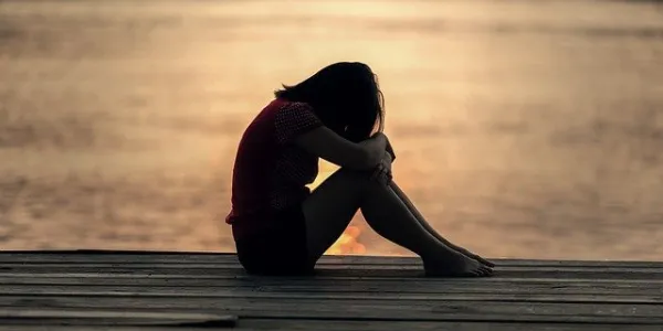 Niña triste sentada frente al atardecer