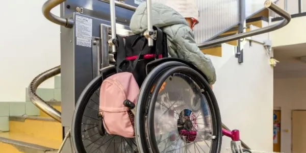 Mujer con discapacidad en silla de ruedas bajando las escaleras por un elevador adaptado