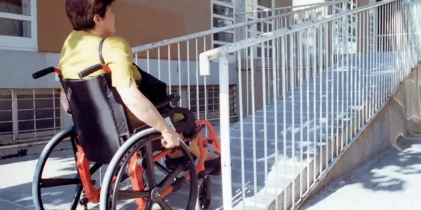 Una mujer en silla de ruedas accede al portal de un edificio de viviendas.
