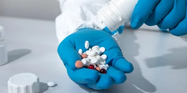 Mano de un sanitario con guantes azules sosteniendo un puñado de pastillas de colores