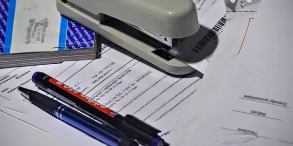 Imagen de folios en una mesa con bolis y grapadora