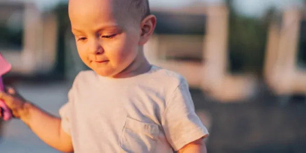 Un niño caucásico de pie en la playa soleada y mirando hacia abajo