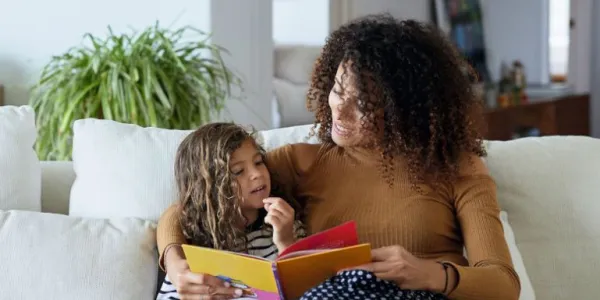Madre con una hija en el sofá leyendo un cuento
