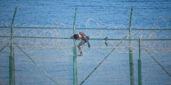 Uno de los 153 migrantes, que han entrado en Ceuta saltando su doble valla en la primera incursión en grupo en un año, se aferra a las concertinas