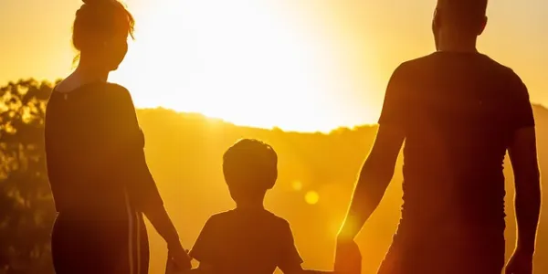Familia de un padre, hijo y madre de espaldas en una puesta de sol