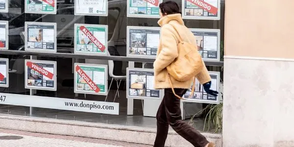 Una joven camina ante el escaparate de una agencia inmobiliaria