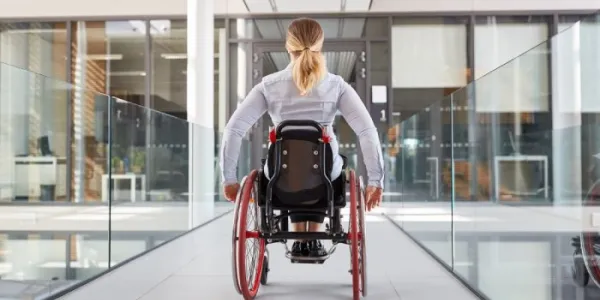 Una mujer avanza con su silla de ruedas por una ofician acristalada 