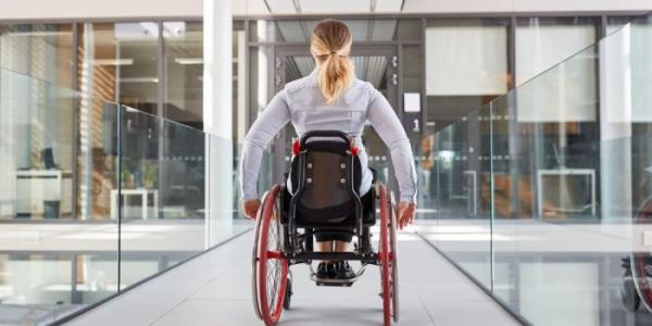 Una mujer avanza con su silla de ruedas por una ofician acristalada 