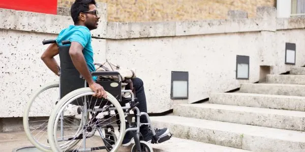Hombre con discapacidad en silla de ruedas esperando en la parte inferior de una escalera