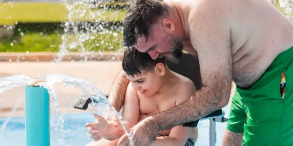 Padre e hijo con parálisis cerebral jugando al agua en la piscina