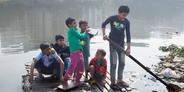  Niños cruzando un lago contaminado en una balsa casera en Dhaka, Bangladesh.