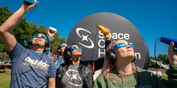 Un grupo de personas con discapacidad visual utilizando dispositivos para oír el eclipse anular de 2023 desde Houston