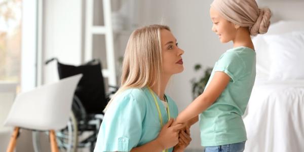 Una profesional sanitaria coge las manos a un niño con cáncer