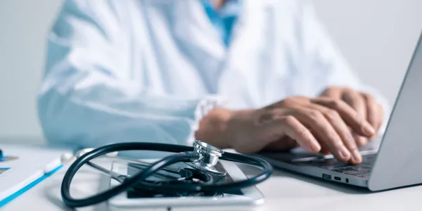 Un médico equipado con un estetoscopio escribiendo en un ordenador 