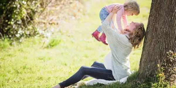 Mujer cogiendo a su hijo en brazos bajo un árbol