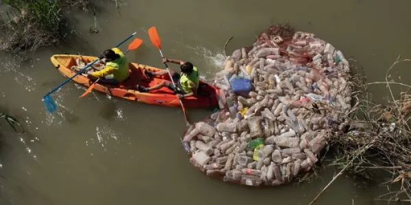 Dos operarios retiran envases de un lugar fluvial