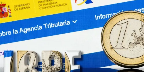 Imagen de una moneda de euro sobre un fondo donde se ve la página web de la Agencia Tributaria