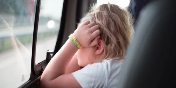 Una niña con las manos en la cara mira por la ventanilla del coche 