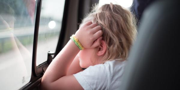 Una niña con las manos en la cara mira por la ventanilla del coche 
