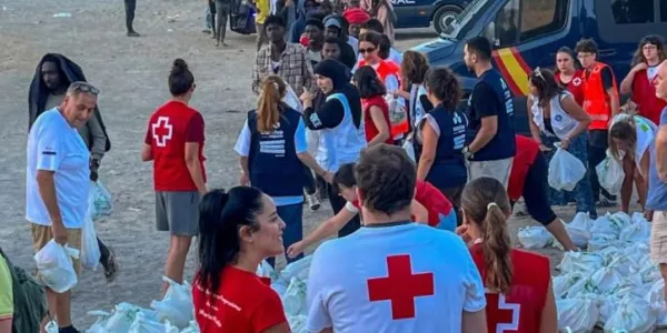 Miembros de la Cruz Roja reparten bolsas de comida a personas migrantes en la playa ‘El Trampolín’ de Ceuta. 