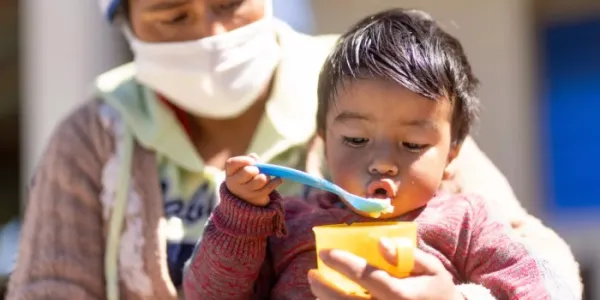 Un niño pequeño come papìlla sentado sobre su madre