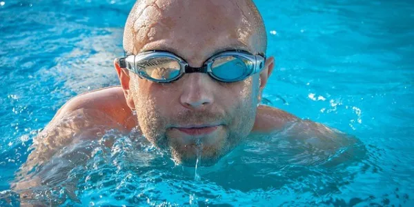 Señor nadando en la piscina con gafas de bucear