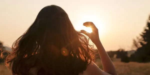 Una mujer observa el sol poniendo su mano como una visera