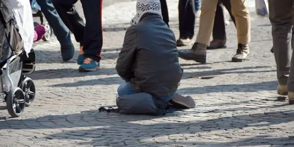 Persona sin recursos arrodillada en la calle pidiendo dinero