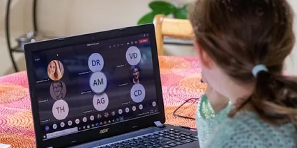 Chica de espaldas teletrabajando con su portátil, en una videollamada