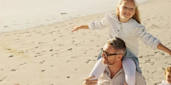 Una niña a hombros de su padre paseando por la playa de vacaciones