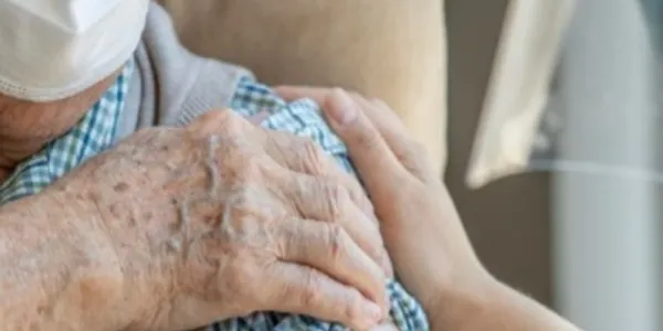 Brazo de un hombre mayor tapándose la marca de una vacuna y una mano de una enfermera ayudándole