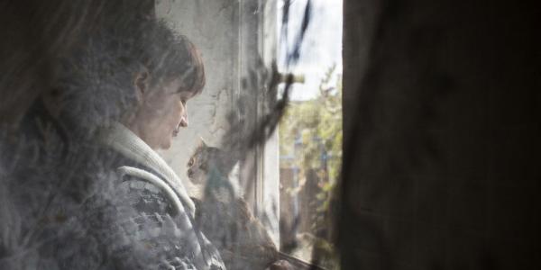 Una mujer que sufre violencia mira por la ventana abrazando a su gato