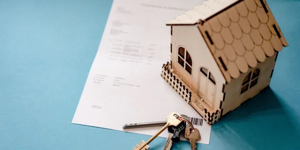 Miniatura de una vivienda en madera con unas llaves de verdad y un contrato de compra