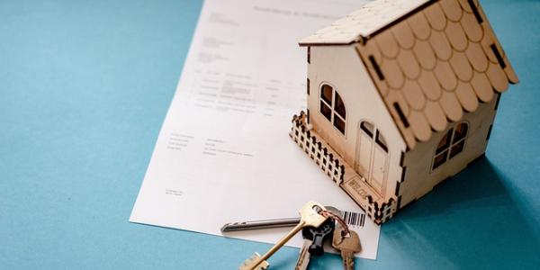 Miniatura de una vivienda en madera con unas llaves de verdad y un contrato de compra