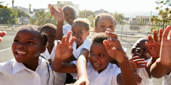 Niños de primaria en el patio de recreo saludando a la cámara